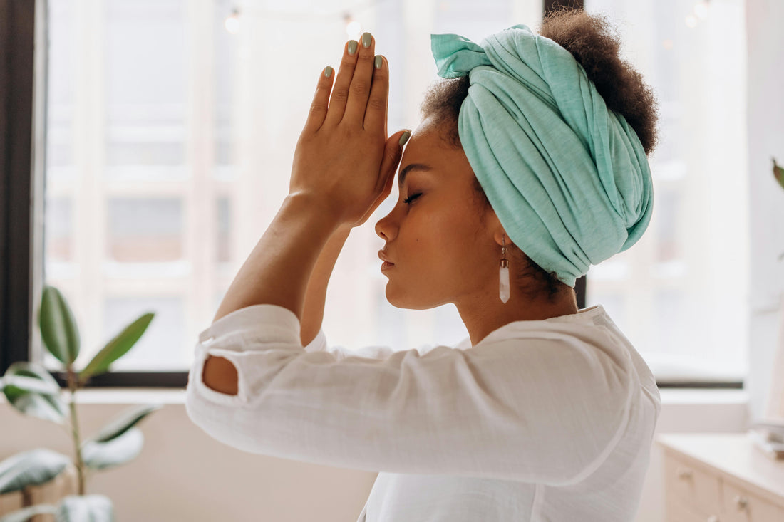 A young woman kneeling in her apartment with prayer hands in front of her face with her eyes closed
