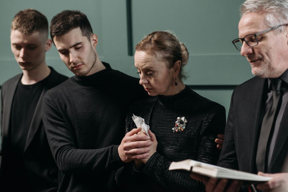 "Grieving woman being comforted by loved ones at a funeral while standing near a coffin."